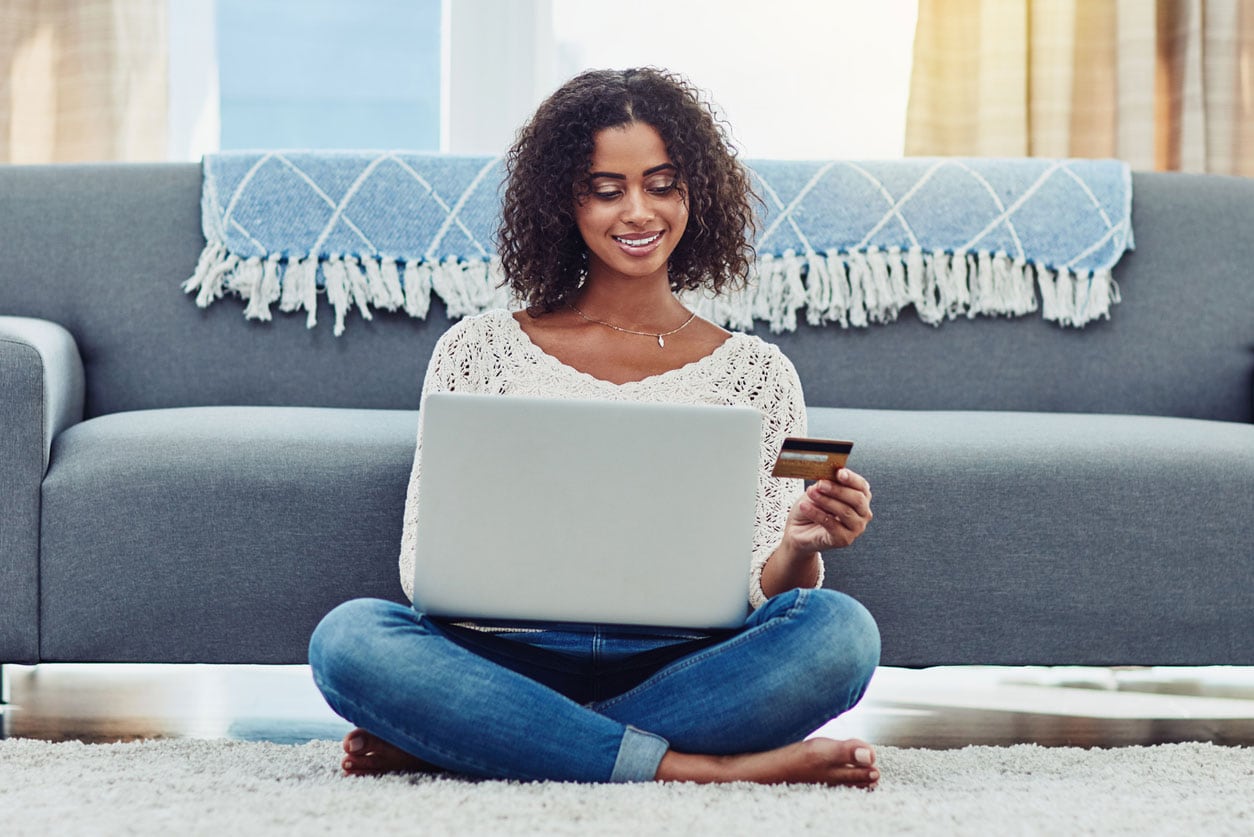 Woman sitting on the floor with her laptop holding a credit card